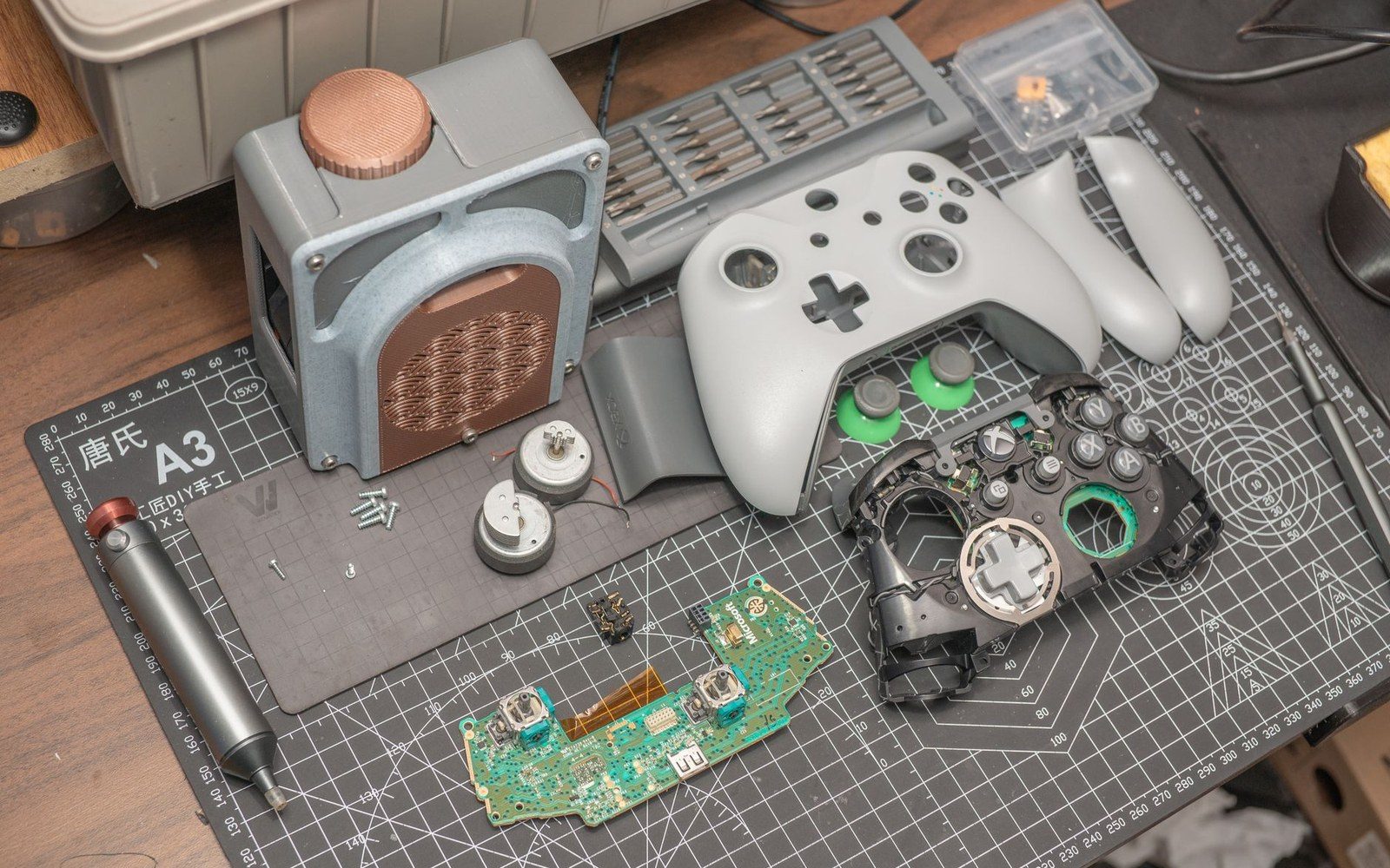 A disassembled game controller with circuit board, plastic shell, and small motors on a cutting mat