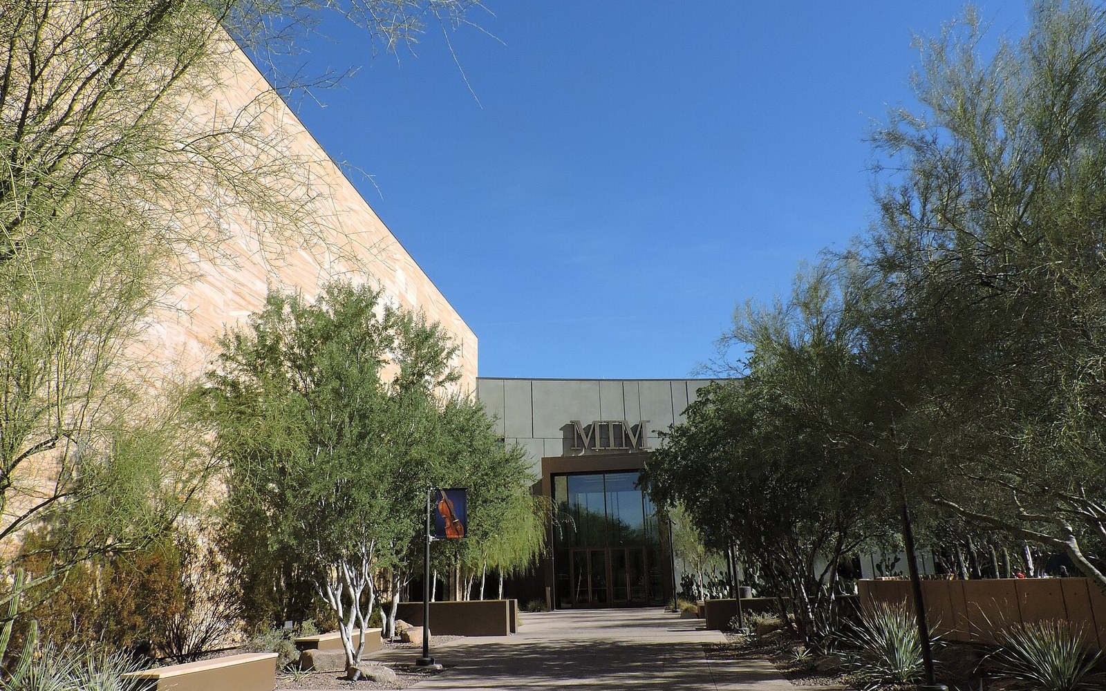 Entrance of the Musical Instrument Museum flanked by desert trees under a clear sky