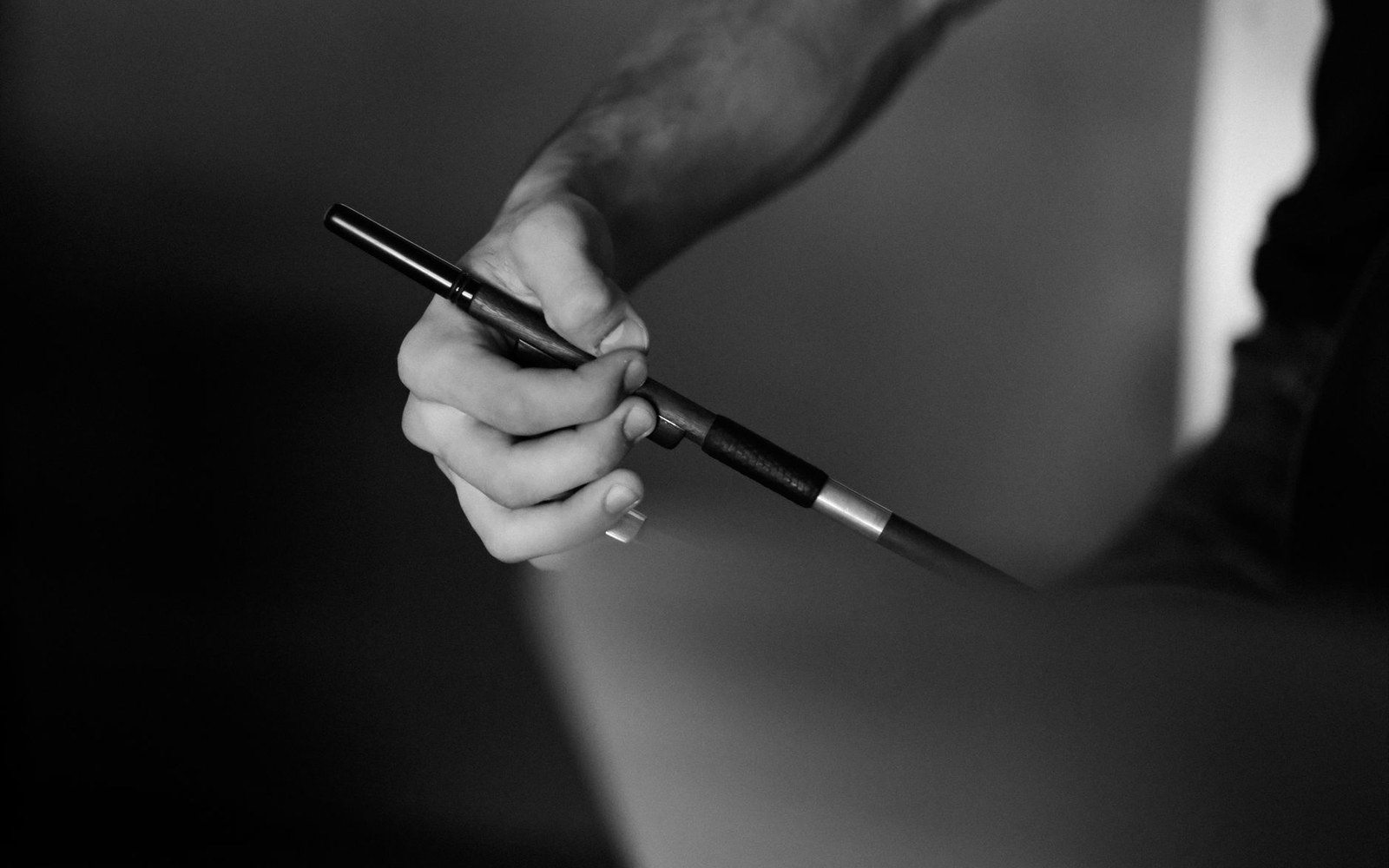 A hand grips a violin bow near its frog in close-up black and white