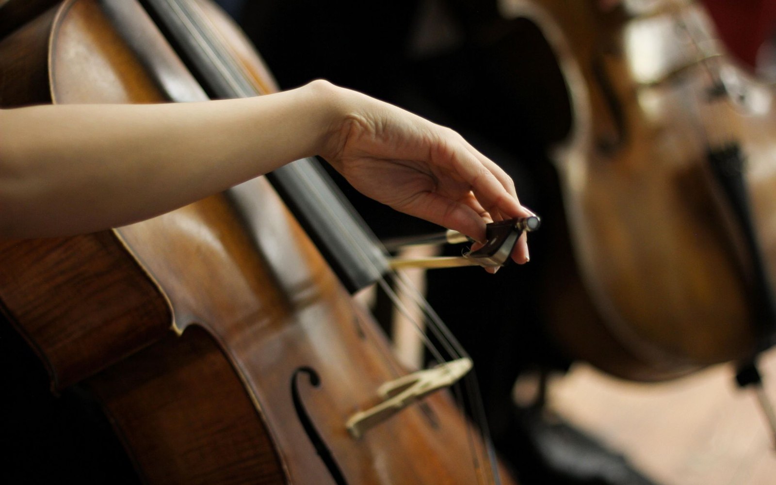 A hand adjusts the frog of a bow resting on a cello's strings