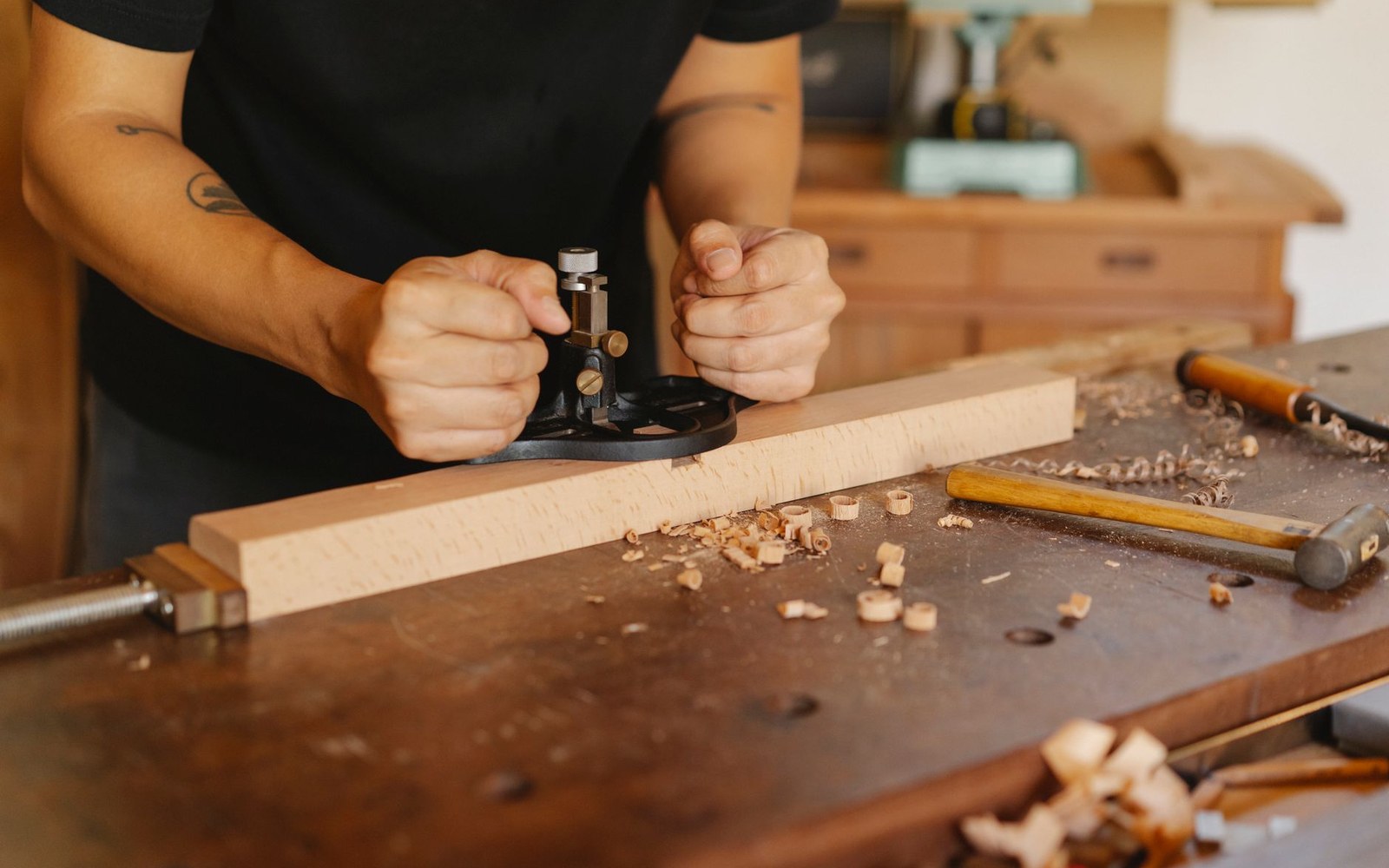 Adult bow maker's hands planing a pernambuco billet on a workshop bench, shavings visible