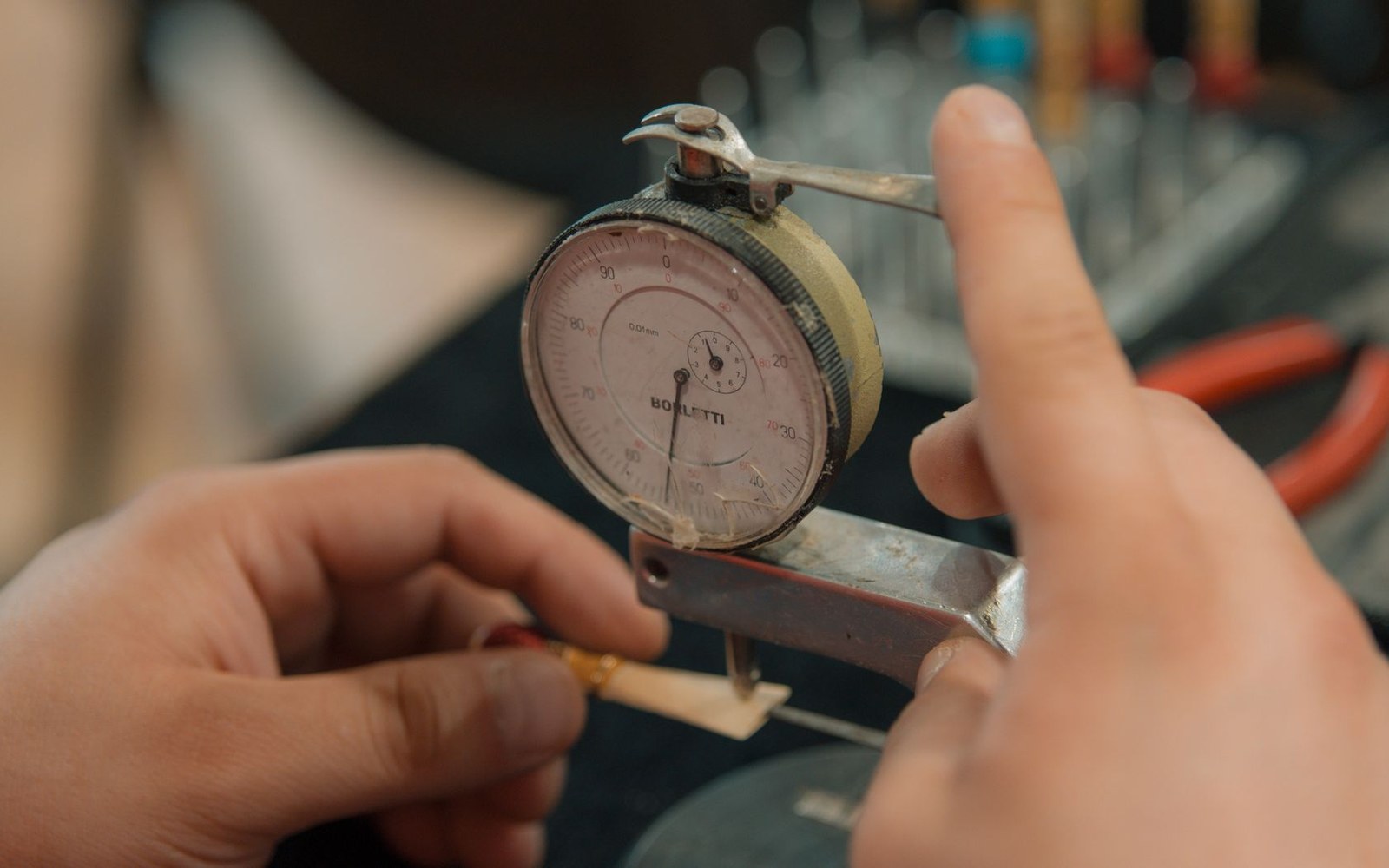 A bow maker's workbench with thumb planes, calipers and a bow-making gauge laid out, one figure visible in background